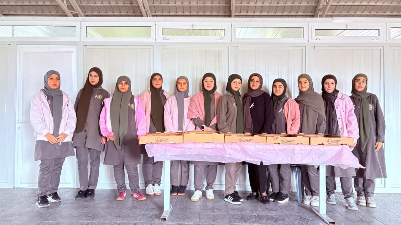 Students in pink and grey stand behind a table of donut boxes.