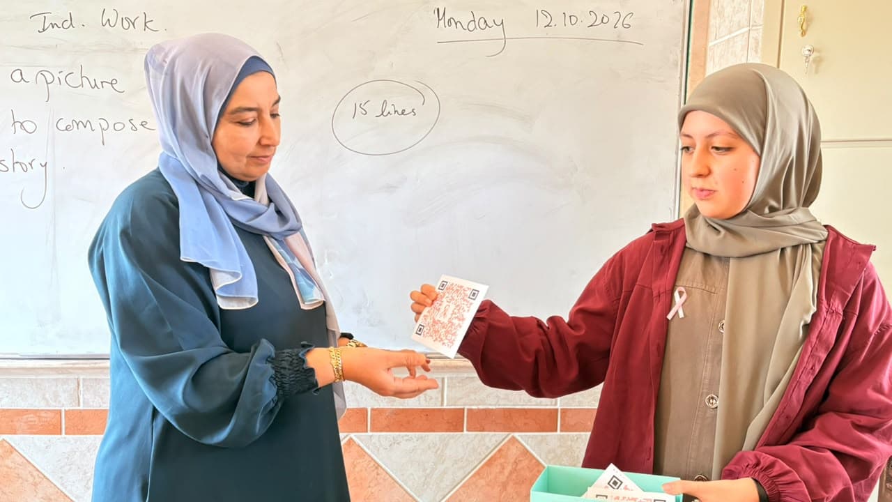 A student hands a QR awareness card to a teacher in class.